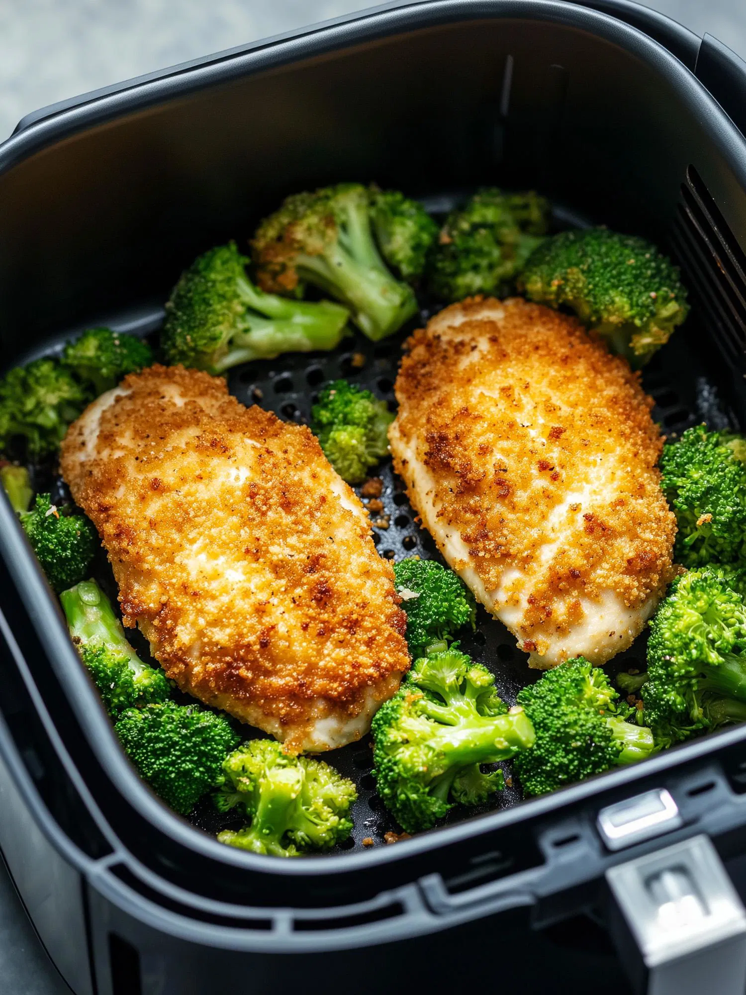 Two golden-brown breaded chicken breasts surrounded by green broccoli florets inside a black air fryer basket.