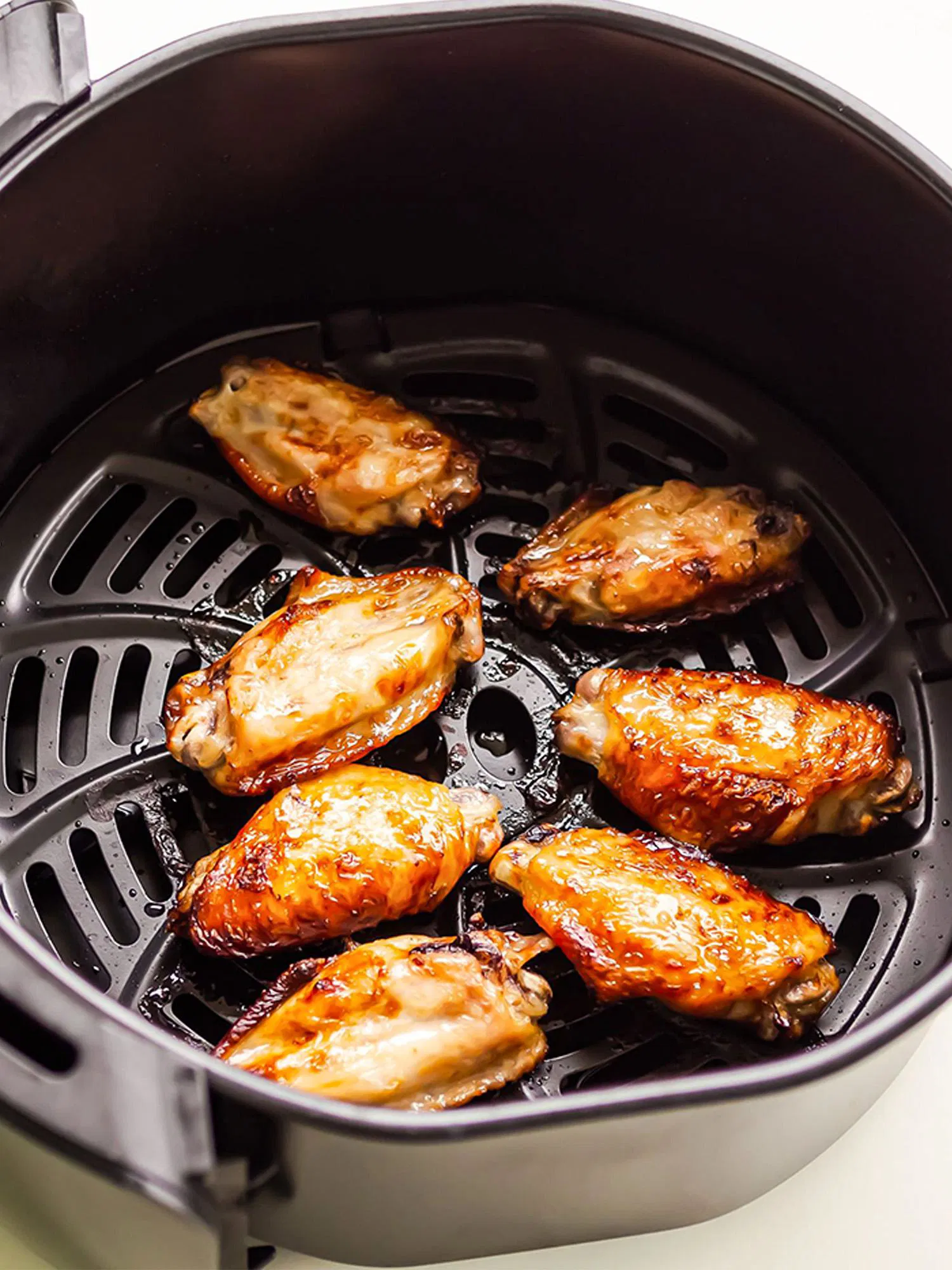 Seven golden-brown chicken wings cooking inside a black air fryer basket