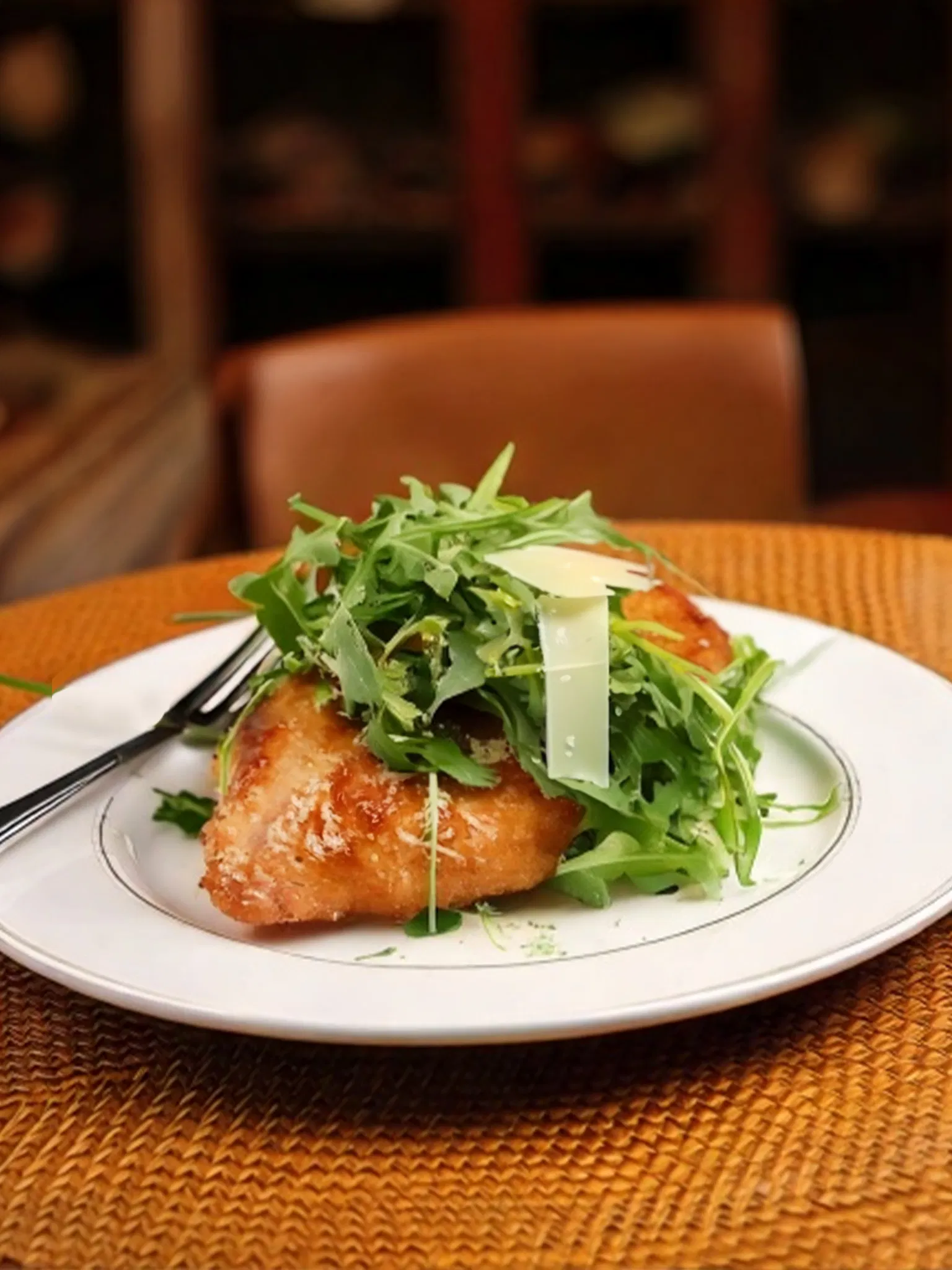 Golden breaded cutlet topped with fresh arugula and shaved parmesan on a white plate