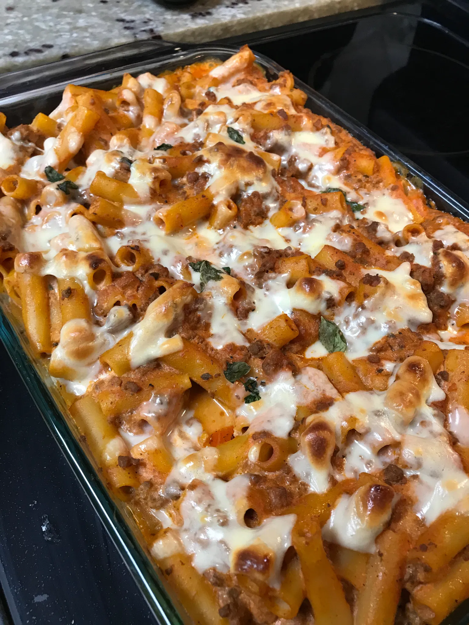 Glass baking dish filled with baked ziti pasta, ground meat, red sauce, and melted white cheese
