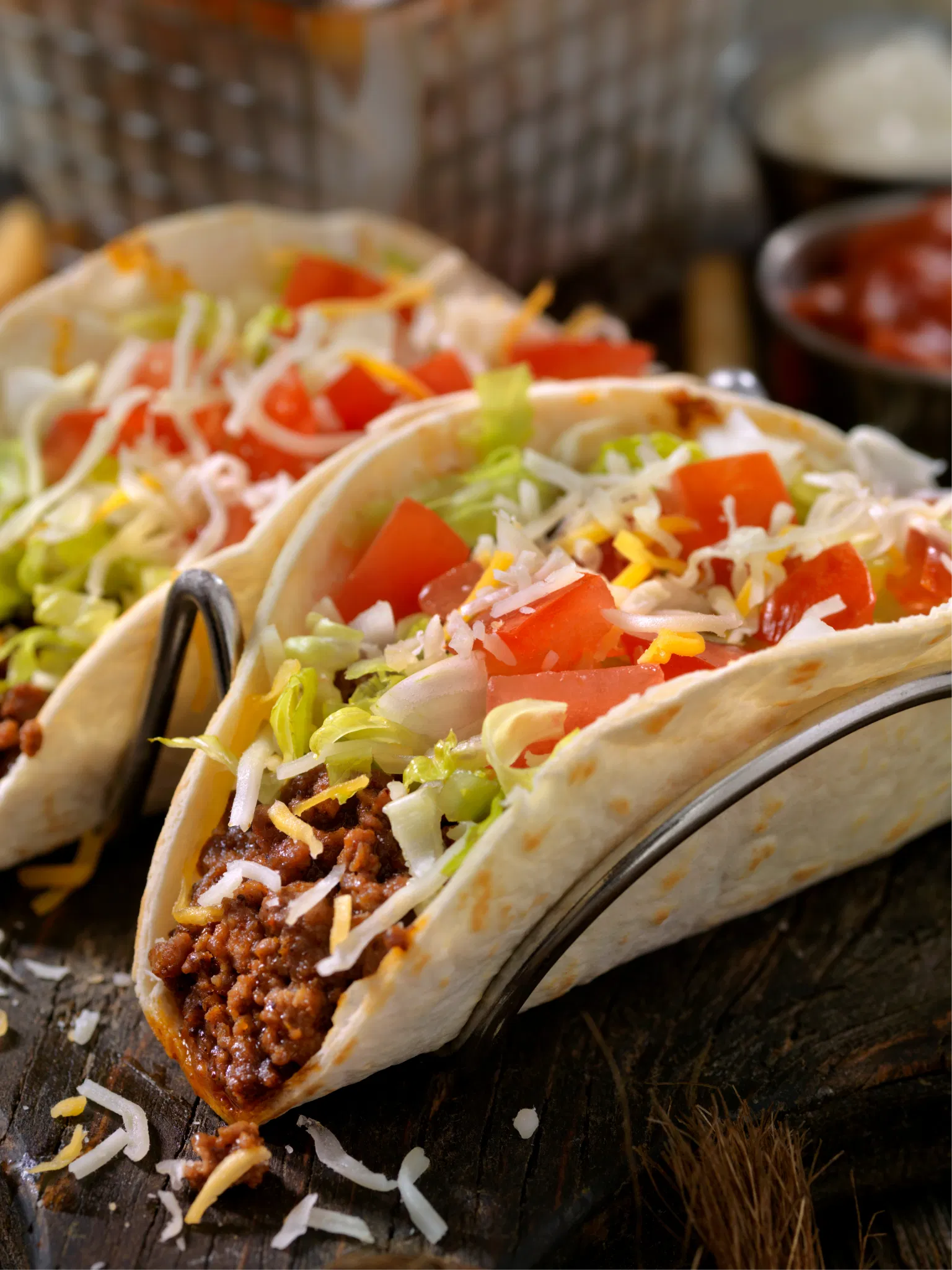 Two soft shell tacos filled with seasoned ground beef, shredded lettuce, diced tomatoes, and cheese in a metal stand