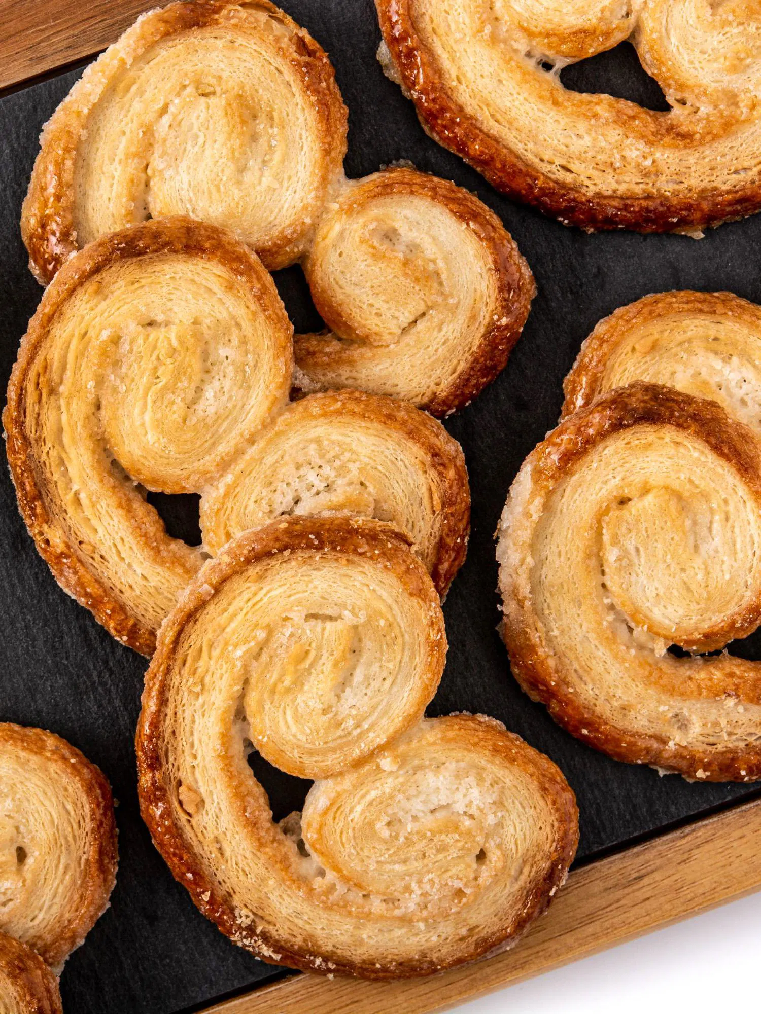 Golden, flaky palmier pastries dusted with sugar arranged on a dark slate serving board