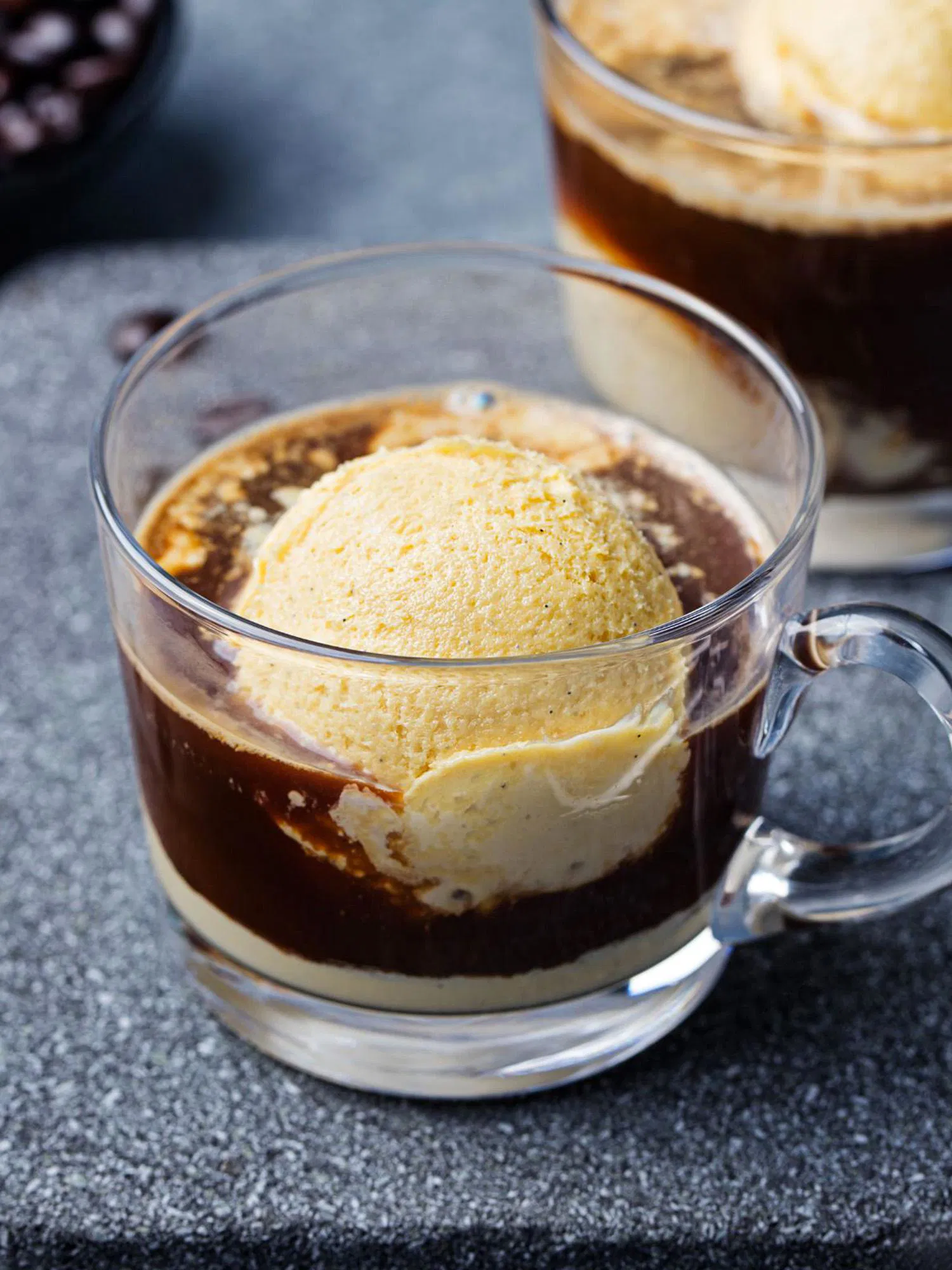 Close-up of a clear glass mug filled with dark espresso and a large scoop of vanilla ice cream melting into the coffee