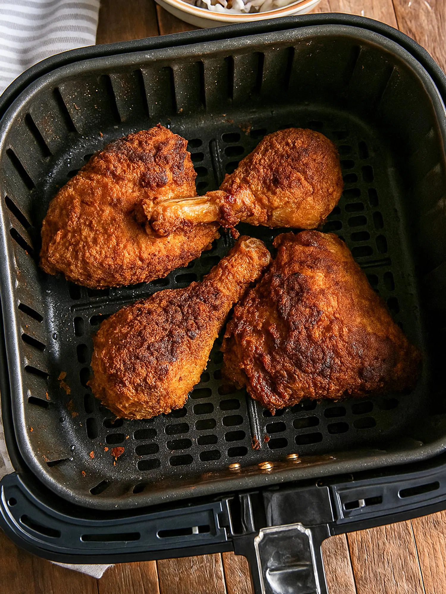 Four pieces of golden-brown crispy fried chicken, including drumsticks and thighs, resting inside a black air fryer basket.