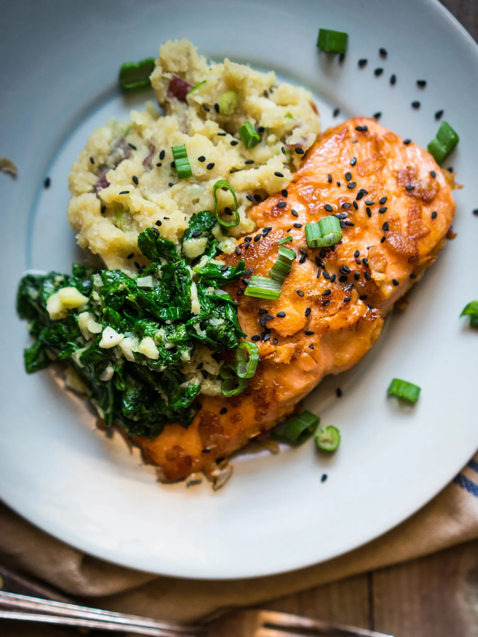 Glazed salmon with mashed potatoes and garlic spinach, garnished with green onions and black sesame seeds