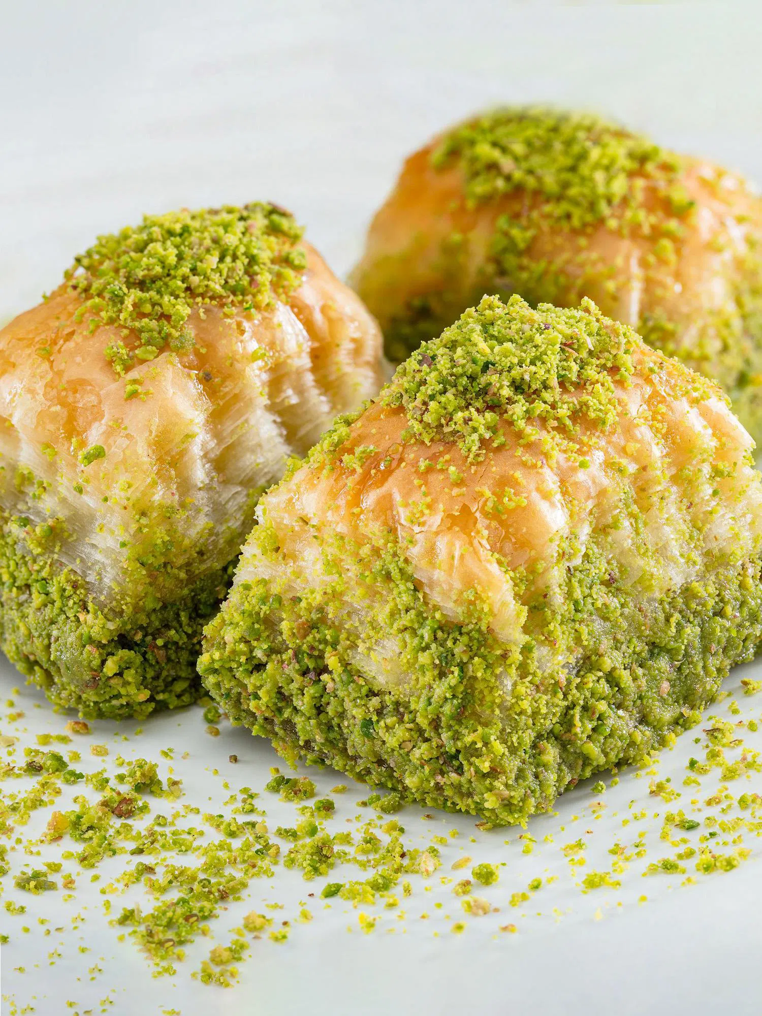 Three square pieces of golden phyllo pastry heavily coated in bright green crushed pistachios on a white surface