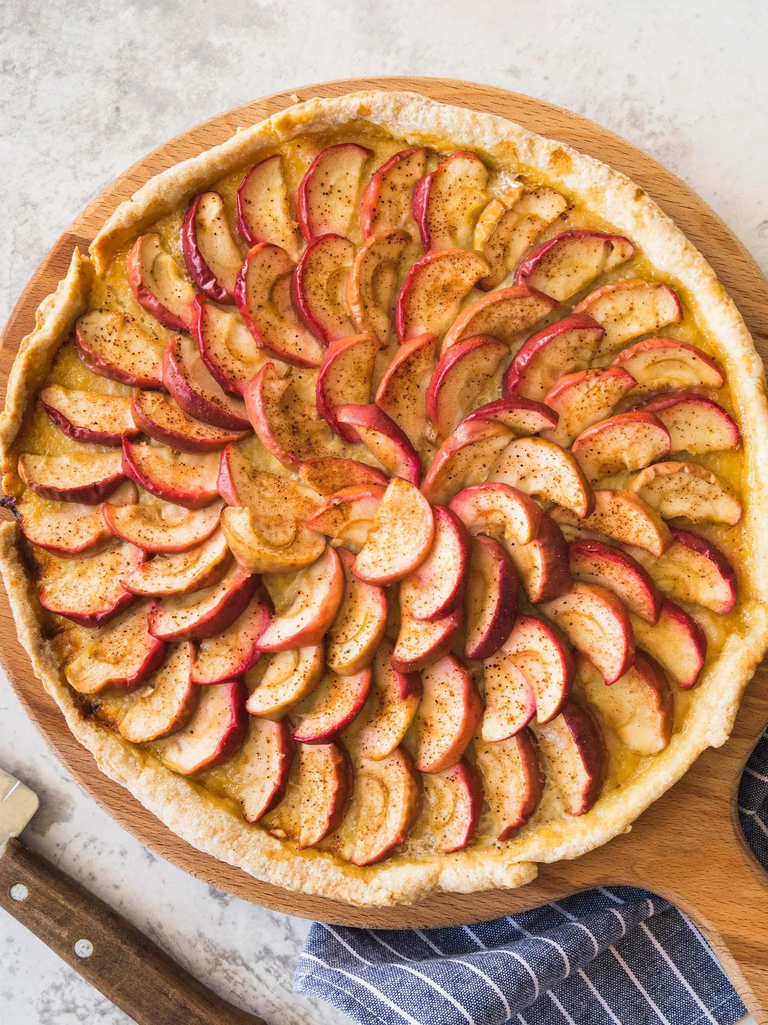 Overhead view of a rustic apple tart on a wooden board, featuring spiraled red apple slices dusted with cinnamon