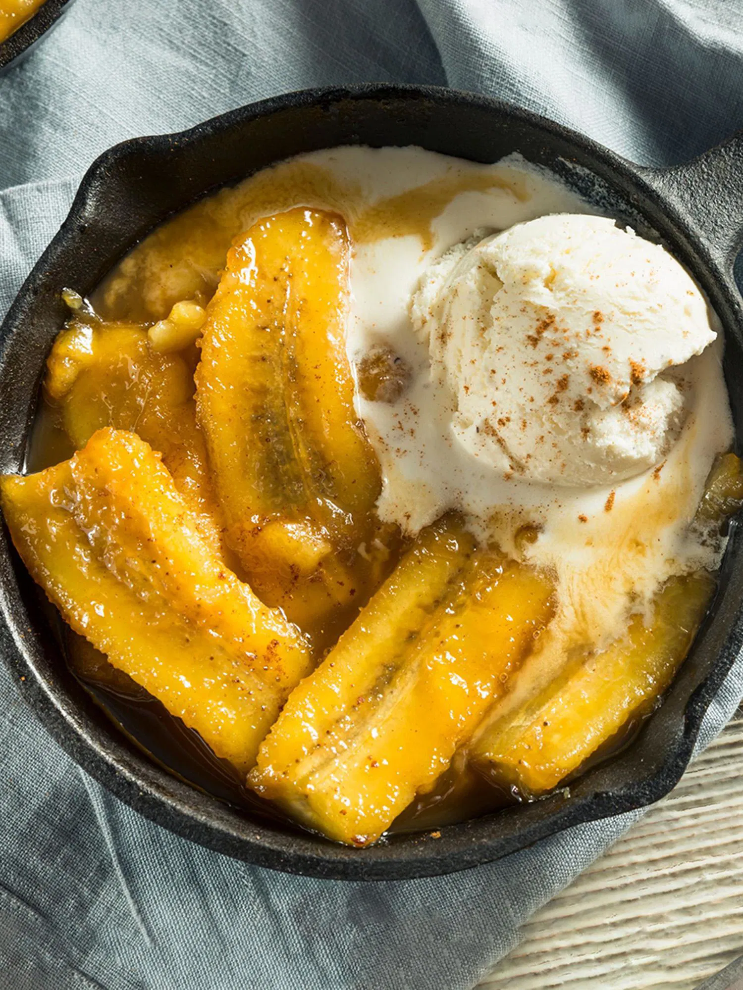 Caramelized bananas in a small cast iron skillet topped with a melting scoop of vanilla ice cream and cinnamon